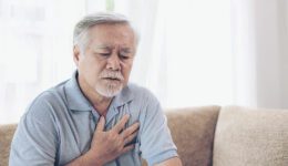 Senior Asian male holding chest because of heart burn.