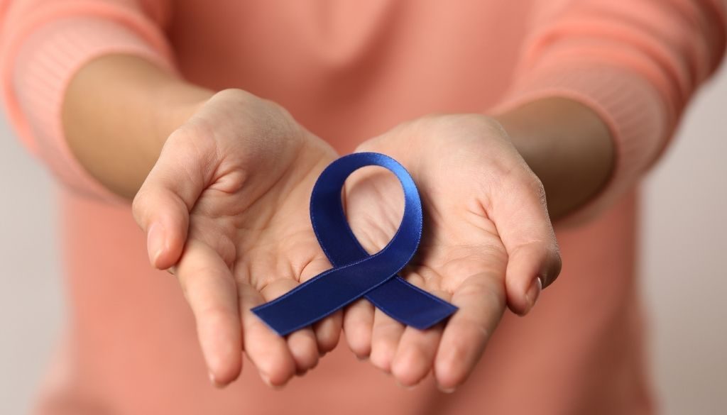 Closeup of a woman holding a small blue awareness ribbon in her hands signs of colon cancer