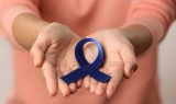 Closeup of a woman holding a small blue awareness ribbon in her hands signs of colon cancer