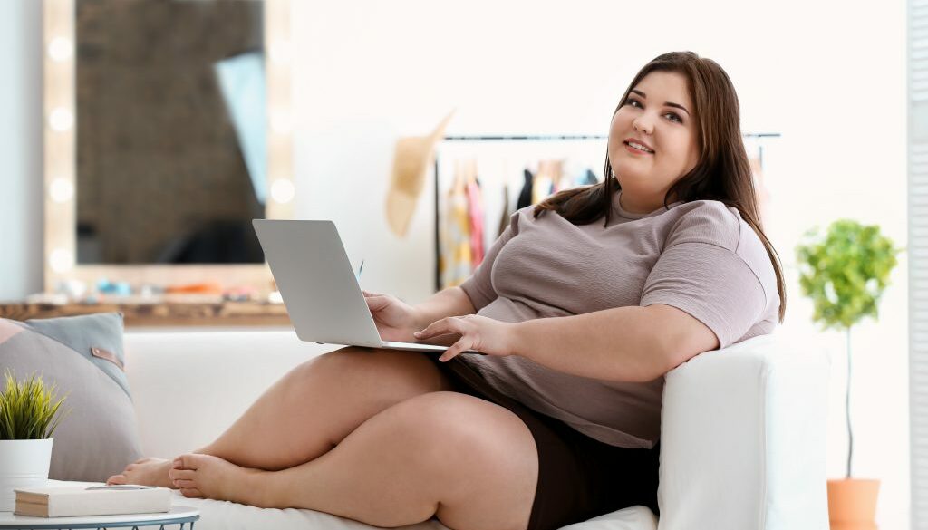 Beautiful overweight woman with laptop indoors
