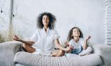 Cute girl and mother meditating on couch