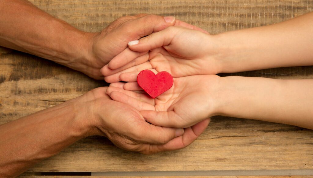 Human hands holding, giving heart isolated on wooden background