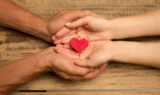 Human hands holding, giving heart isolated on wooden background