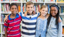 Smiling school kids standing with arm around in library