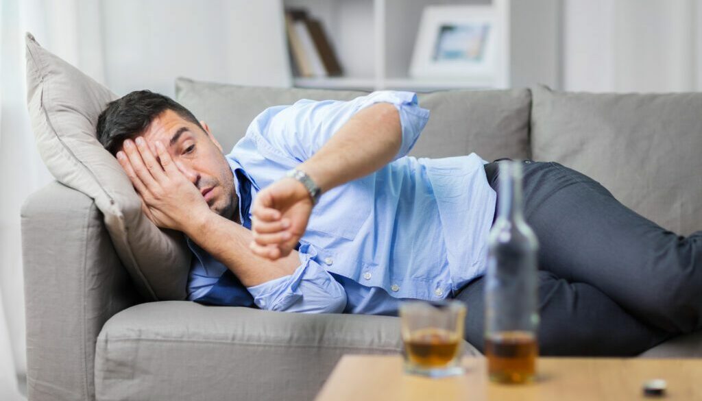 alcoholic lying on sofa and looking at wristwatch