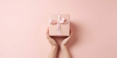 christmas background with hands holding present box on a pink background.
