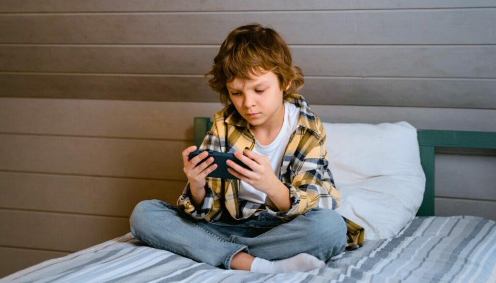 Kid sitting in bed looking at a smartphone and children