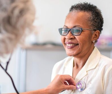 An african american woman smiling while getting her heart rate taken importance of heart screenings
